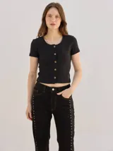 Remera negra de canalé ajustada al cuerpo, de manga corta y cuello redondo, con cierre frontal de botones metálicos.