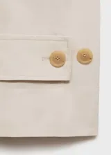 Abrigo largo de diseño oversize en color beige, confeccionado en tejido de algodón con elastano. Presenta cuello alto abotonado, cierre frontal con botones, mangas largas con trabillas en los puños y cinturón tipo batín para ajustar a la cintura. Incluye dos bolsillos laterales.