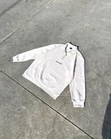 Conjunto de dos piezas compuesto por un buzo de cuello alto con cierre frontal corto y un pantalón tipo jogger de corte relajado. Ambas prendas presentan el logo RonaStudio bordado en color negro y están confeccionadas en algodón premium de tono beige.