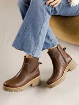 Bota corta de cuero vacuno color marrón, con suela de goma tipo track en tono beige, cierre lateral interno y costuras visibles.
