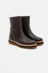 Bota de caña media confeccionada en cuero vacuno texturizado color marrón oscuro. Presenta un diseño minimalista con costuras reforzadas, tirador trasero y una suela de plataforma plana con capas en tonos beige, negro y suela.