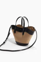 Bolso tipo canasta con cuerpo de tela color camel y detalles, asas y bandolera de cuero sintético negro. Presenta costuras blancas contrastantes en todos los bordes. Incluye asas de mano y una correa ajustable y desmontable para llevar al hombro o cruzado.