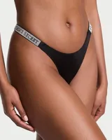Panty tipo tanga negra con tiras laterales brillantes decoradas con pedrería y la inscripción de la marca Victoria's Secret.