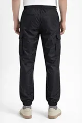 Pantalón cargo de nylon color beige, con elástico en la cintura y en los puños. Presenta bolsillos laterales con solapa y un logo de goma aplicado en uno de ellos.