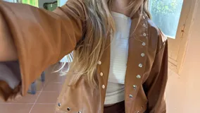 Campera corta de ecocuero color camel, con diseño de cuello solapa y cierre frontal con botones metálicos a presión. Presenta detalles de tachas metálicas a lo largo de la solapa y en el ruedo.