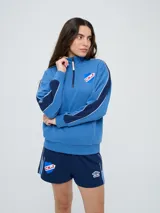 Buzo de felpa azul marino con medio cierre, cuello alto, bandas laterales en tono rosado y bolsillo frontal tipo canguro. Presenta el logo de Umbro y el escudo del Club Nacional de Football bordados.