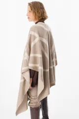 Ruana de tejido de punto con diseño geométrico de líneas curvas en tonos beige y visón. Presenta una caída fluida y envolvente, ideal para usar como capa sobre otras prendas.