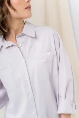 Camisa verde pastel de algodón, corte oversize, con cuello camisero, cierre con botones, mangas largas con puños con volados de encaje blanco, dos bolsillos frontales con solapa y ruedo irregular. 