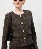 Casaqueto femenino de corte recto y largo corto, confeccionado en tejido estructurado con textura chevron. Presenta escote redondeado sin cuello, manga larga, cierre frontal con botones visibles y bolsillos decorativos con solapa.