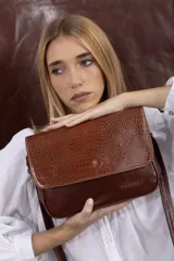 Cartera bandolera de cuero vacuno color bordó, con solapa frontal de textura símil cocodrilo y detalles de costuras pespunteadas en blanco. Cuenta con correa ajustable y cierre superior.