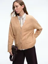 Cardigan de punto color beige con cierre frontal de botones, cuello en V y dos bolsillos delanteros. Presenta mangas largas con puños acanalados y un diseño de corte holgado.