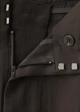 Pantalón de corte recto y tiro medio color marrón oscuro, confeccionado en lyocell, con detalle de pinzas delanteras, trabillas para cinto, bolsillos laterales y bolsillos de ribete en la parte posterior. Cierre frontal con botón y cremallera.