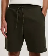 Bermuda masculina de algodón con felpa, color negro, corte slim fit. Presenta cintura elástica con cordón ajustable, bolsillos y etiqueta aplicada.