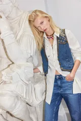 Chaleco de denim azul con bordados metalizados y pedrería en la parte superior delantera, escote en V y cierre frontal con botones metálicos.