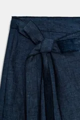 Pantalón azul de tiro medio con corte ancho, cierre frontal cruzado tipo pareo con botón interior y lazada.