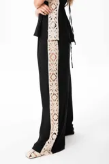 Pantalón sastrero de lino color negro con una guarda lateral de broderie color crudo que recorre el lateral desde la cintura hasta el bajo. El pantalón es de corte ancho y fluido.
