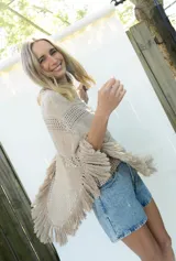 Poncho de tejido de algodón color beige claro, con diseño de punto calado y flecos en el borde inferior.
