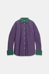 Camisa de popelín de corte oversize, color violeta con cuello y puños anchos a contraste en color verde. Presenta cierre frontal con botones, mangas largas y un bolsillo de parche en el pecho.