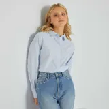 Camisa celeste a rayas verticales blancas, de corte recto, manga larga y cuello italiano.