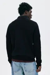 Buzo negro de tejido punto, con cuello alto y cierre metálico parcial frontal. Presenta un corte recto y mangas largas.