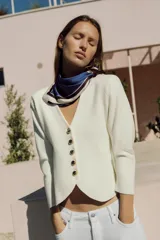 Chaqueta de punto color negro con escote en V, mangas largas y cierre frontal con botones dorados. Presenta un diseño de bajo asimétrico.