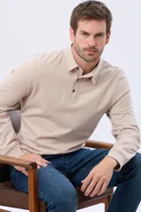 Remera polo de manga larga confeccionada en tejido jersey, con cuello clásico y cierre frontal de tres botones. Presenta un diseño liso con un pequeño logo bordado en el pecho y una etiqueta decorativa en el ruedo.