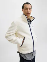 Campera de tejido tipo teddy color crema, con cuello alto, cierre frontal completo y ribetes en color azul marino. Presenta bolsillos laterales con cierre y bordado en el pecho.
