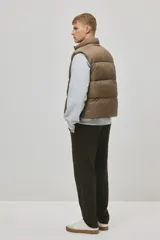 Chaleco acolchado color tostado, de nylon guateado, repelente al agua y rompevientos. Cuenta con cuello elevado, cierre bidireccional con protección para el mentón, bolsillos laterales con cierre y un bolsillo interior con botón a presión. El bajo es ajustable con cordón elástico y topes.