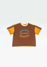 Remera marrón con mangas cortas color mostaza, cuello redondo color crema y estampado frontal con la frase "Vigilante Peacemaker Quotes".