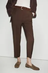 Pantalón de tiro alto en color beige, con diseño de pinzas frontales y bolsillos laterales. Incluye un cinturón a contraste en tono marrón con hebilla metálica y cierre frontal con cremallera y gancho.
