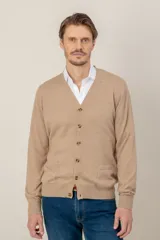 Cardigan de punto en lana merino color beige, con cuello en V, cierre frontal de botones y dos bolsillos delanteros tipo parche.