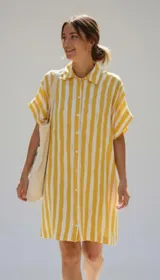 Vestido camisero de silueta relajada, con cuello clásico, cierre frontal de botones y mangas cortas con dobladillo. Presenta un estampado de cuadrícula irregular en color rojo sobre fondo blanco.