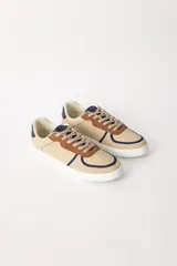 Zapatillas urbanas color beige con detalles en marrón y azul marino, cordones marrones y suela blanca.