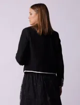 Chaqueta de tweed negra marca Nanette, con escote a la base, abertura central con botones, bolsillos delanteros, aplique de botones perlados en los puños, ribete en contraste blanco y forro interno.