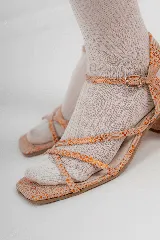 Sandalias de tacón bajo con diseño de tiras finas cruzadas en el empeine y cierre de hebilla en el tobillo. Presentan una puntera cuadrada y acabado con textura efecto reptil en tonos metalizados.