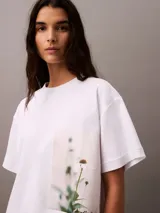 Remera blanca de algodón con corte cropped y mangas cortas. Presenta un estampado fotográfico floral de Calvin Klein en el lateral.