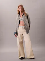 Pantalón chino de Calvin Klein, color beige, con diseño de pierna súper ancha, tiro alto, cinco bolsillos y cierre frontal con botón y cremallera.