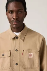 Campera estilo trucker de color marrón claro, confeccionada en gabardina resistente. Cuenta con cuello clásico, cierre frontal de botones metálicos, bolsillos frontales con solapa y bolsillos laterales ribeteados.