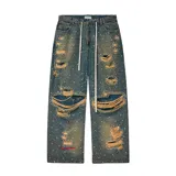 Pantalón de jean azul de corte baggy, con efecto desgastado, roturas grandes y múltiples apliques de pedrería o tachas brillantes por toda la prenda. Posee cordón blanco en la cintura en lugar de un cinturón tradicional.