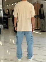 Remera oversize color beige, con mangas cortas y cuello redondo. Presenta un diseño estampado con texto en la parte trasera y lateral, de corte holgado y estilo urbano.