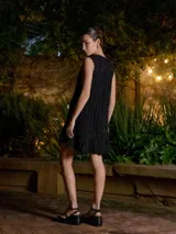 Vestido corto de punto sin mangas, con diseño de rayas verticales en tonos azul marino y negro con hilos de lurex. Presenta un corte recto con un volado en el ruedo que aporta movimiento.