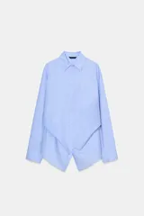 Camisa de popelín color celeste claro, con cuello solapa, manga larga y detalle de pliegue asimétrico en el bajo frontal.