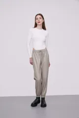 Pantalón tipo babucha de eco cuero color cemento, con cintura elástica y cordón de ajuste, bolsillos laterales y puños elásticos en los tobillos.