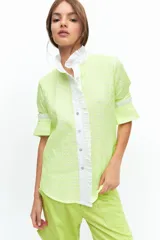 Camisa de manga larga confeccionada en broderie de algodón con bordados en hilo flúo color naranja. Presenta cuello mao, cartera frontal con volados y puños con volados.