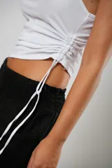 Top blanco de morley fino, con un solo hombro, ojales a ambos costados y cordones regulables que permiten ajustar el largo.