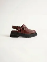 Zueco de cuero vacuno color bordó, con diseño de punta redondeada, detalle de tira con tachas metálicas y herrajes en tono oro viejo. Cuenta con un taco cuadrado de 4,5 cm y suela de cuero.