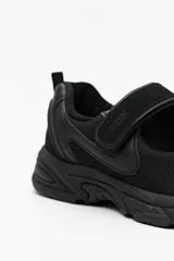 Zapatillas deportivas negras con suela blanca de 4cm de alto y tira ajustable con velcro.