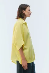 Camisa oversize blanca de lino, con corte cuadrado, mangas raglán cortas con puños anchos, aberturas laterales y cierre frontal de botones.