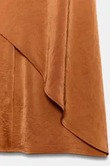 Pantalón fluido de tiro alto en color tostado, con pernera ancha y volantes superpuestos en la parte delantera. Cuenta con cierre frontal con cremallera, botón interior y gancho.