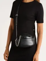 Cartera tipo bandolera de silueta redondeada, confeccionada en cuero sintético negro. Presenta un bolsillo frontal con textura efecto cocodrilo, detalle de cadena metálica plateada decorativa y correa ajustable con la misma textura. Incluye logo de la marca en la parte frontal.